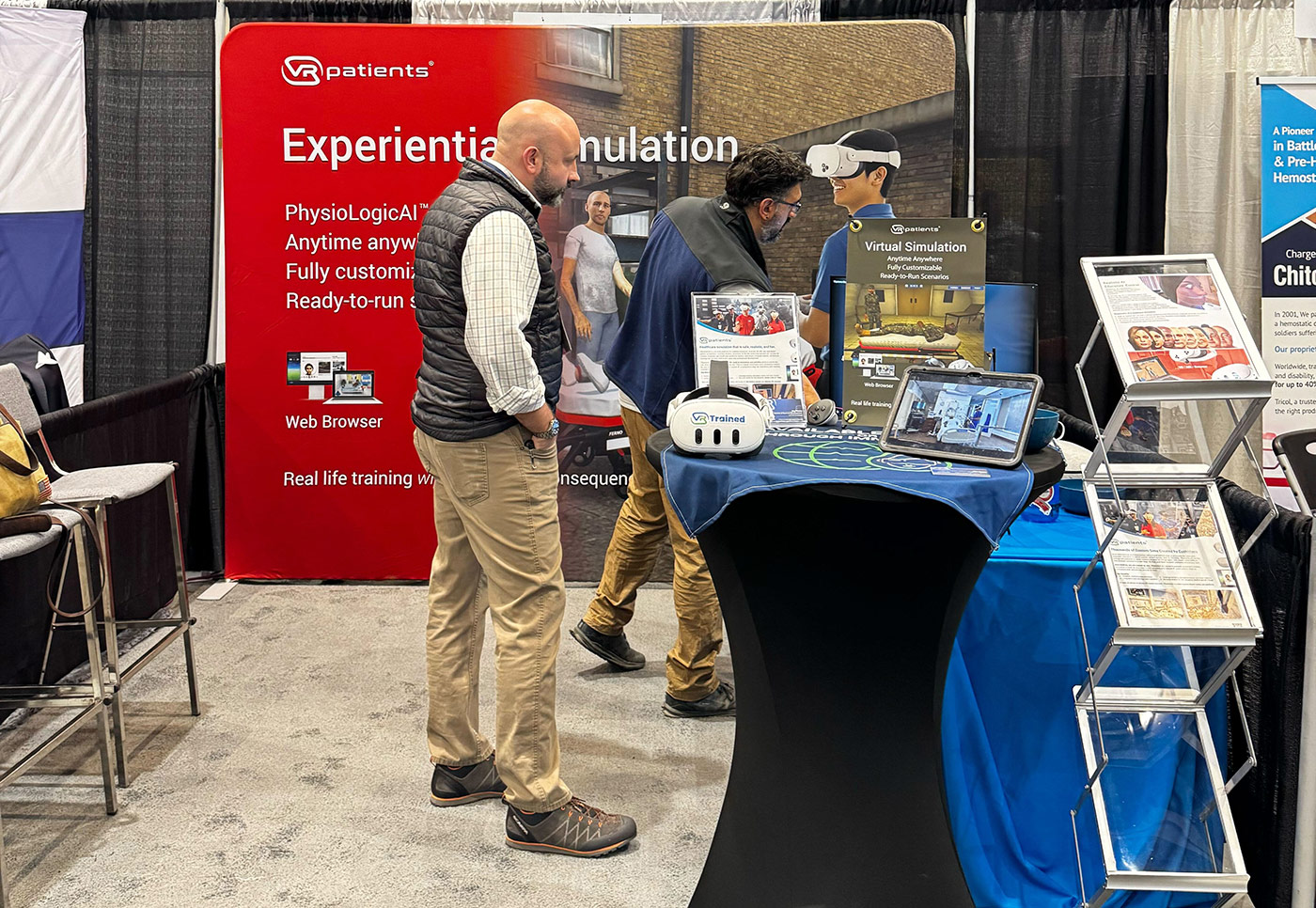 Exhibition booth showcasing virtual simulation and training tools with two men talking near a red banner that says 'Experiential Simulation'.